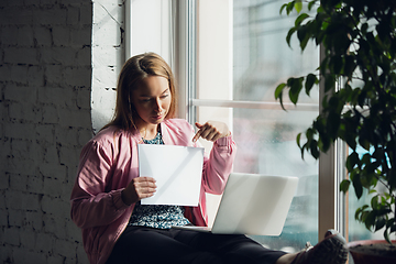 Image showing Young woman, businesswoman working or studying at home holding white sheet, whiteboard. Attented, concentrated. Copyspace. Top view.