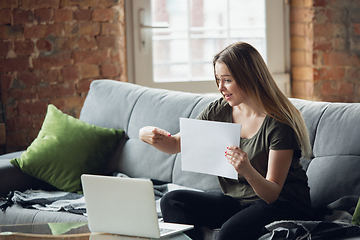 Image showing Young woman, businesswoman working or studying at home, looking on computer screen, monitor, holding white sheet, whiteboard. Attented, concentrated. Copyspace. Top view.