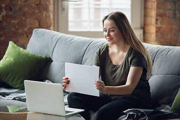 Image showing Young woman, businesswoman working or studying at home, looking on computer screen, monitor, holding white sheet, whiteboard. Attented, concentrated. Copyspace. Top view.