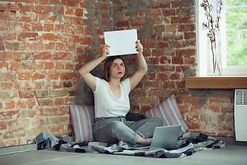 Image showing Young woman, businesswoman working or studying at home, looking on computer screen, monitor, holding white sheet, whiteboard. Attented, concentrated. Copyspace. Top view.