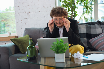 Image showing Young man in pajama and jacket working on a computer, laptop. Remote office during coronavirus, fun and comfortable work in underpants