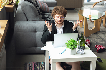 Image showing Young man without pants but in jacket working on a computer, laptop. Remote office during coronavirus, fun and comfortable work in underpants