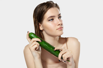 Image showing Youth secrets. Close up of beautiful young woman with cucumber over white background. Cosmetics and makeup, natural and eco treatment, skin care.