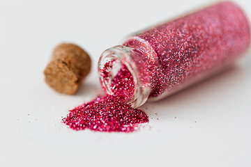 Image showing pink red glitters poured from small glass bottle