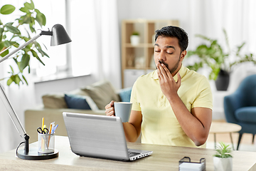 Image showing man with laptop and coffee yawning at home office