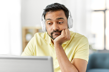 Image showing bored man in headphones with laptop works at home