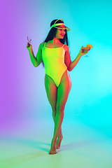 Image showing Beautiful girl in fashionable swimsuit isolated on gradient studio background in neon light. Summer, resort, fashion and weekend concept