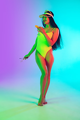 Image showing Beautiful girl in fashionable swimsuit isolated on gradient studio background in neon light. Summer, resort, fashion and weekend concept