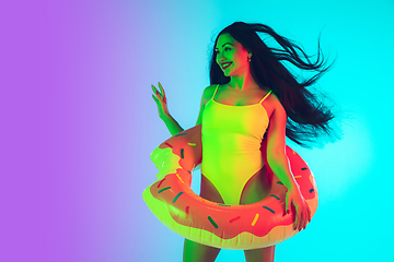 Image showing Beautiful girl in fashionable swimsuit isolated on gradient studio background in neon light. Summer, resort, fashion and weekend concept