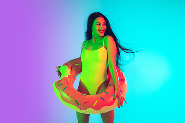 Image showing Beautiful girl in fashionable swimsuit isolated on gradient studio background in neon light. Summer, resort, fashion and weekend concept