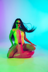 Image showing Beautiful girl in fashionable swimsuit isolated on gradient studio background in neon light. Summer, resort, fashion and weekend concept