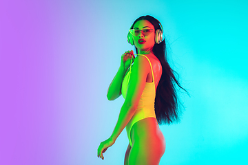 Image showing Beautiful girl in fashionable swimsuit isolated on gradient studio background in neon light. Summer, resort, fashion and weekend concept