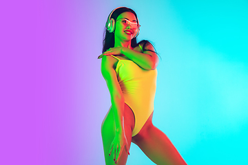 Image showing Beautiful girl in fashionable swimsuit isolated on gradient studio background in neon light. Summer, resort, fashion and weekend concept