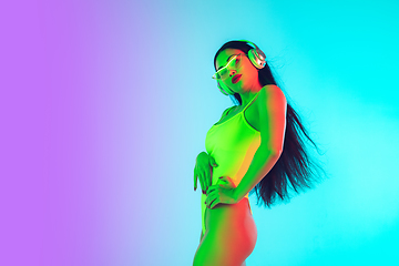 Image showing Beautiful girl in fashionable swimsuit isolated on gradient studio background in neon light. Summer, resort, fashion and weekend concept