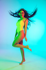 Image showing Beautiful girl in fashionable swimsuit isolated on gradient studio background in neon light. Summer, resort, fashion and weekend concept