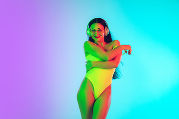 Image showing Beautiful girl in fashionable swimsuit isolated on gradient studio background in neon light. Summer, resort, fashion and weekend concept