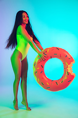 Image showing Beautiful girl in fashionable swimsuit isolated on gradient studio background in neon light. Summer, resort, fashion and weekend concept