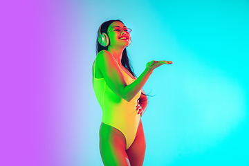 Image showing Beautiful girl in fashionable swimsuit isolated on gradient studio background in neon light. Summer, resort, fashion and weekend concept