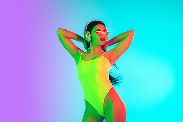 Image showing Beautiful girl in fashionable swimsuit isolated on gradient studio background in neon light. Summer, resort, fashion and weekend concept