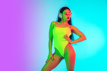 Image showing Beautiful girl in fashionable swimsuit isolated on gradient studio background in neon light. Summer, resort, fashion and weekend concept