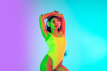 Image showing Beautiful girl in fashionable swimsuit isolated on gradient studio background in neon light. Summer, resort, fashion and weekend concept