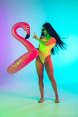 Image showing Beautiful girl in fashionable swimsuit isolated on gradient studio background in neon light. Summer, resort, fashion and weekend concept