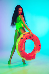 Image showing Beautiful girl in fashionable swimsuit isolated on gradient studio background in neon light. Summer, resort, fashion and weekend concept