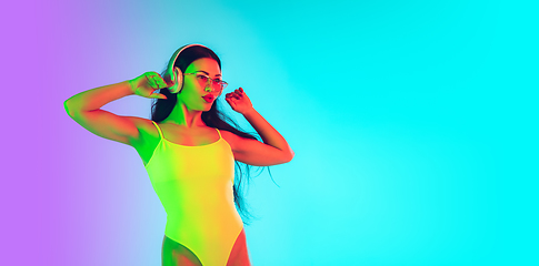 Image showing Beautiful girl in fashionable swimsuit isolated on gradient studio background in neon light. Summer, resort, fashion and weekend concept. Flyer with copyspace.