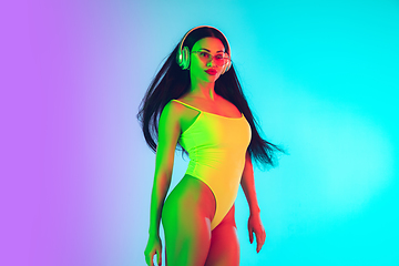 Image showing Beautiful girl in fashionable swimsuit isolated on gradient studio background in neon light. Summer, resort, fashion and weekend concept