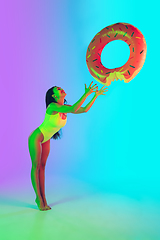 Image showing Beautiful girl in fashionable swimsuit isolated on gradient studio background in neon light. Summer, resort, fashion and weekend concept