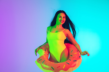 Image showing Beautiful girl in fashionable swimsuit isolated on gradient studio background in neon light. Summer, resort, fashion and weekend concept