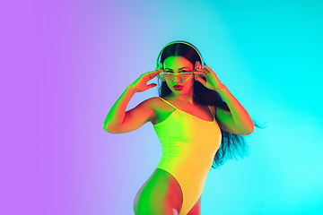 Image showing Beautiful girl in fashionable swimsuit isolated on gradient studio background in neon light. Summer, resort, fashion and weekend concept