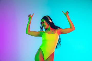 Image showing Beautiful girl in fashionable swimsuit isolated on gradient studio background in neon light. Summer, resort, fashion and weekend concept