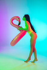 Image showing Beautiful girl in fashionable swimsuit isolated on gradient studio background in neon light. Summer, resort, fashion and weekend concept