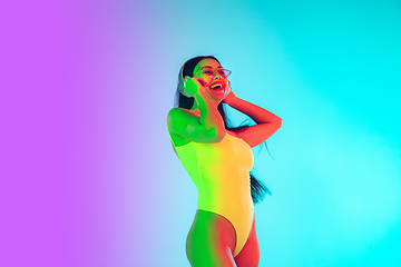 Image showing Beautiful girl in fashionable swimsuit isolated on gradient studio background in neon light. Summer, resort, fashion and weekend concept