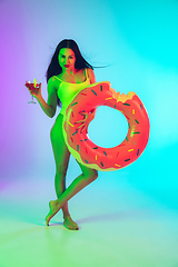 Image showing Beautiful girl in fashionable swimsuit isolated on gradient studio background in neon light. Summer, resort, fashion and weekend concept