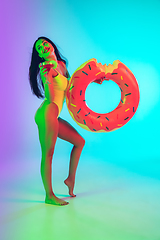 Image showing Beautiful girl in fashionable swimsuit isolated on gradient studio background in neon light. Summer, resort, fashion and weekend concept