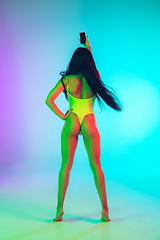 Image showing Beautiful girl in fashionable swimsuit isolated on gradient studio background in neon light. Summer, resort, fashion and weekend concept