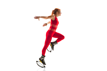 Image showing Beautiful redhead woman in a red sportswear jumping in a kangoo jumps shoes isolated on white studio background.