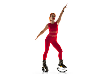 Image showing Beautiful redhead woman in a red sportswear jumping in a kangoo jumps shoes isolated on white studio background.