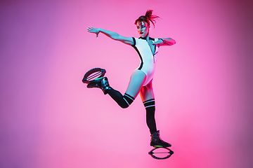 Image showing Beautiful redhead woman in a white sportswear jumping in a kangoo jumps shoes isolated on gradient studio background in neon light