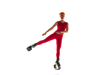 Image showing Beautiful redhead woman in a red sportswear jumping in a kangoo jumps shoes isolated on white studio background.