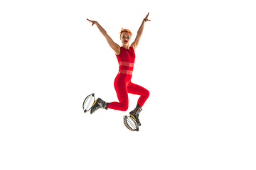 Image showing Beautiful redhead woman in a red sportswear jumping in a kangoo jumps shoes isolated on white studio background.
