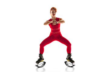 Image showing Beautiful redhead woman in a red sportswear jumping in a kangoo jumps shoes isolated on white studio background.