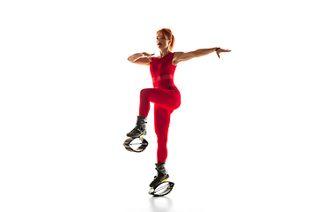 Image showing Beautiful redhead woman in a red sportswear jumping in a kangoo jumps shoes isolated on white studio background.