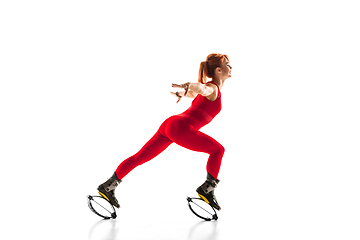 Image showing Beautiful redhead woman in a red sportswear jumping in a kangoo jumps shoes isolated on white studio background.