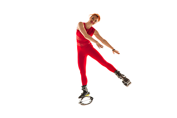 Image showing Beautiful redhead woman in a red sportswear jumping in a kangoo jumps shoes isolated on white studio background.