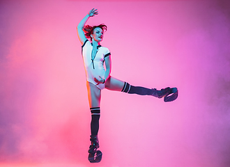 Image showing Beautiful redhead woman in a white sportswear jumping in a kangoo jumps shoes isolated on gradient studio background in neon light