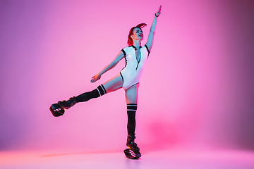 Image showing Beautiful redhead woman in a white sportswear jumping in a kangoo jumps shoes isolated on gradient studio background in neon light