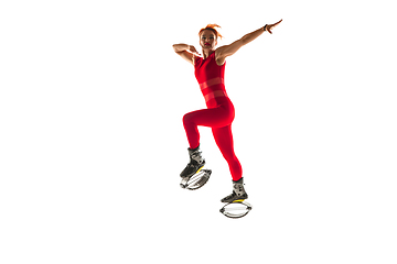 Image showing Beautiful redhead woman in a red sportswear jumping in a kangoo jumps shoes isolated on white studio background.